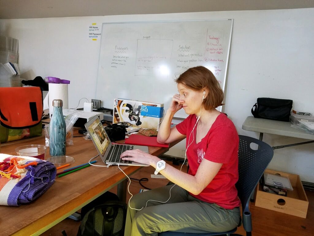 a frustrated looking woman sitting in front of a laptop at a cluttered desk