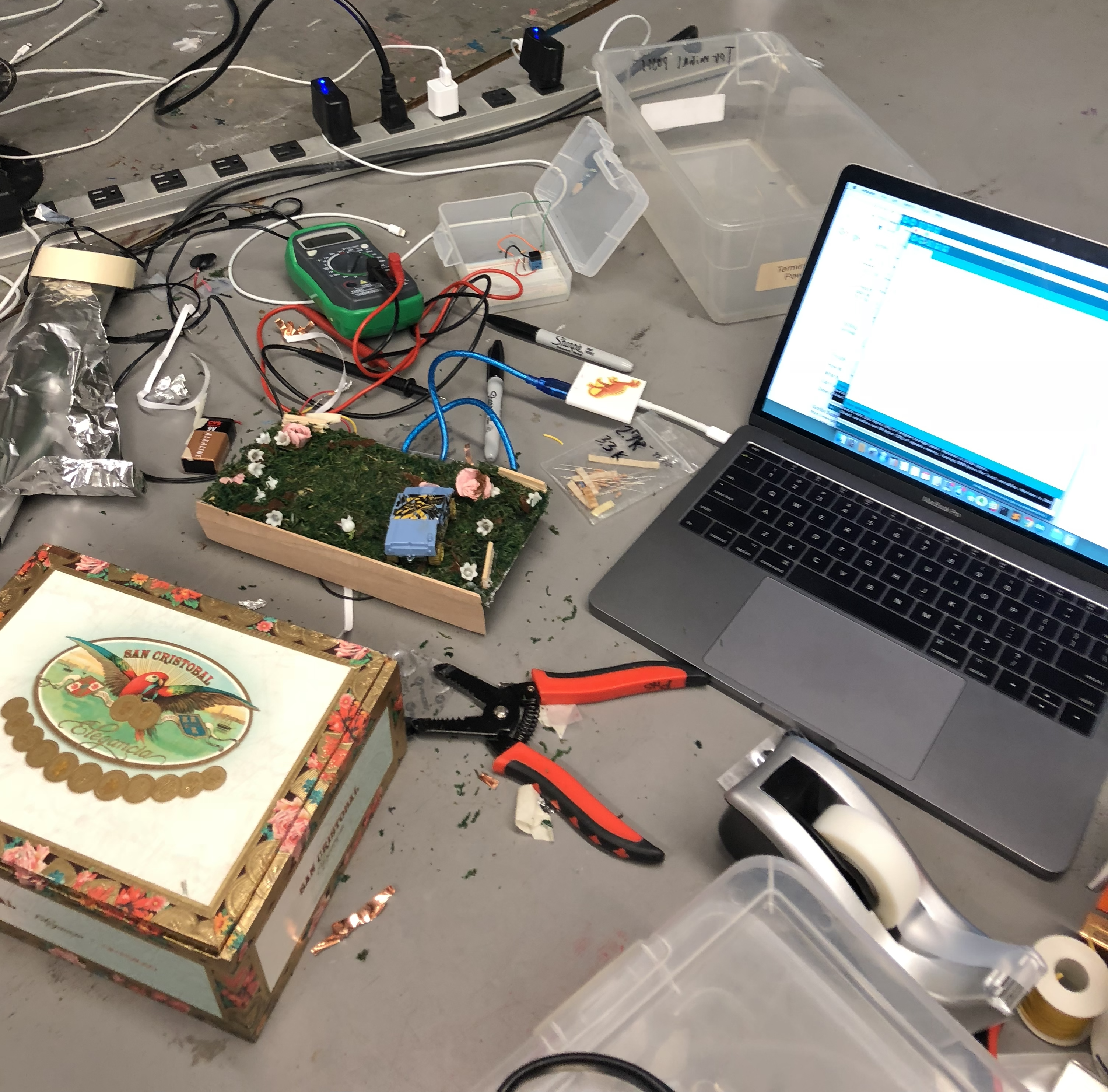 a tabletop with a computer, a micricontroller, hand tools, and a diorama of a garden