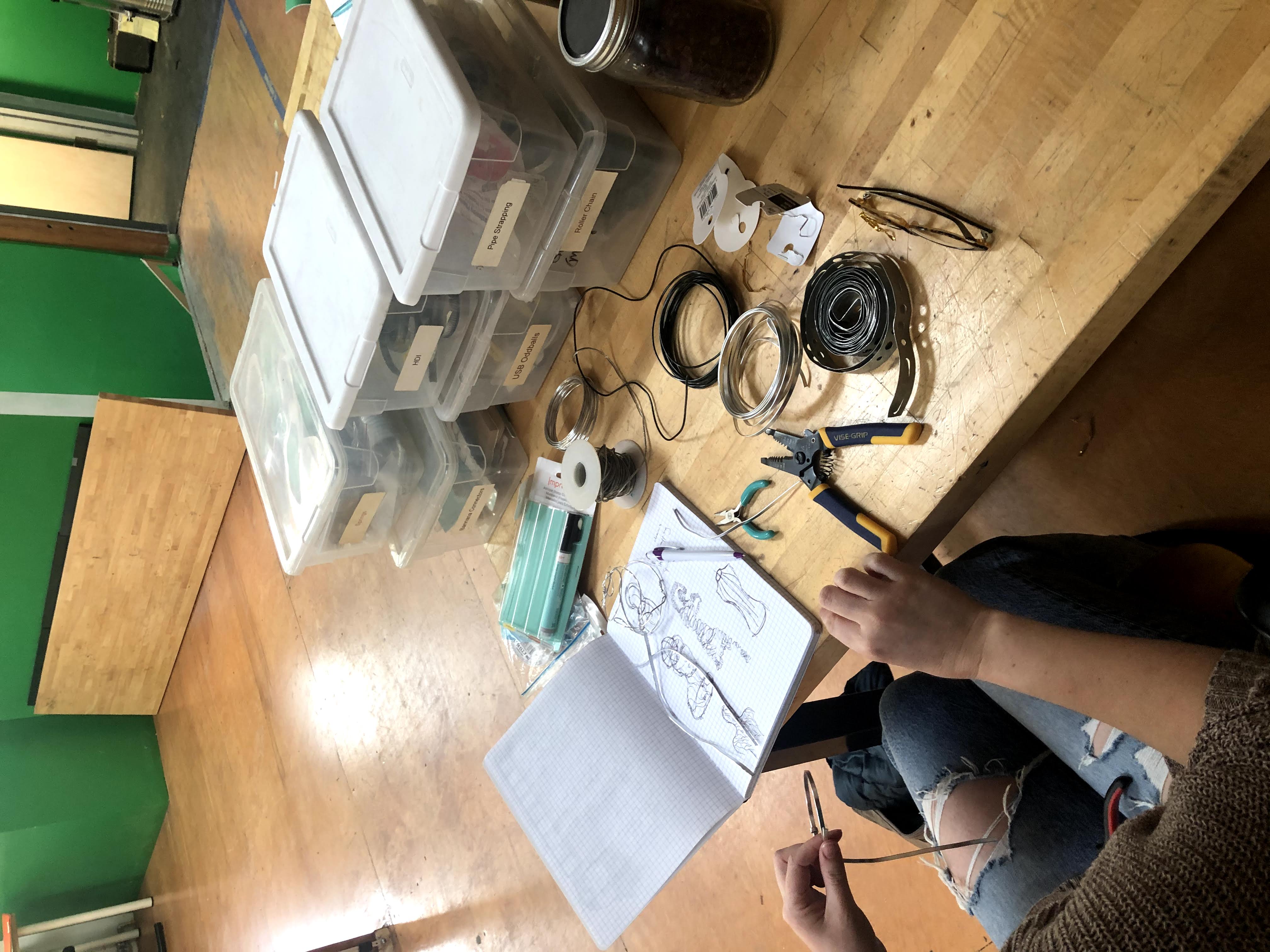 a desk with metalworking supplies and a person handling a piece of wire