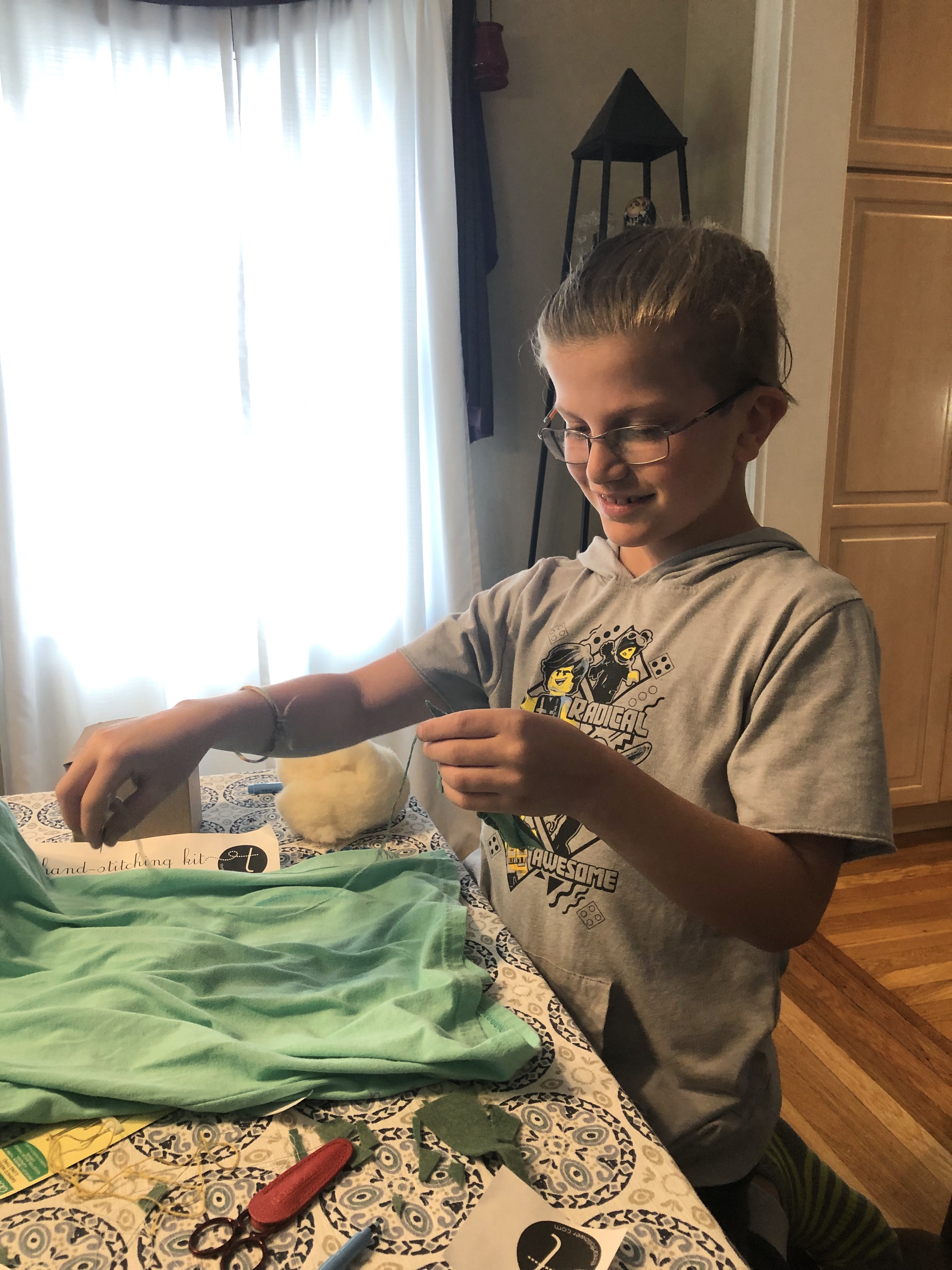 a 9 year old child at a table with fabric and a needle and thread in hand