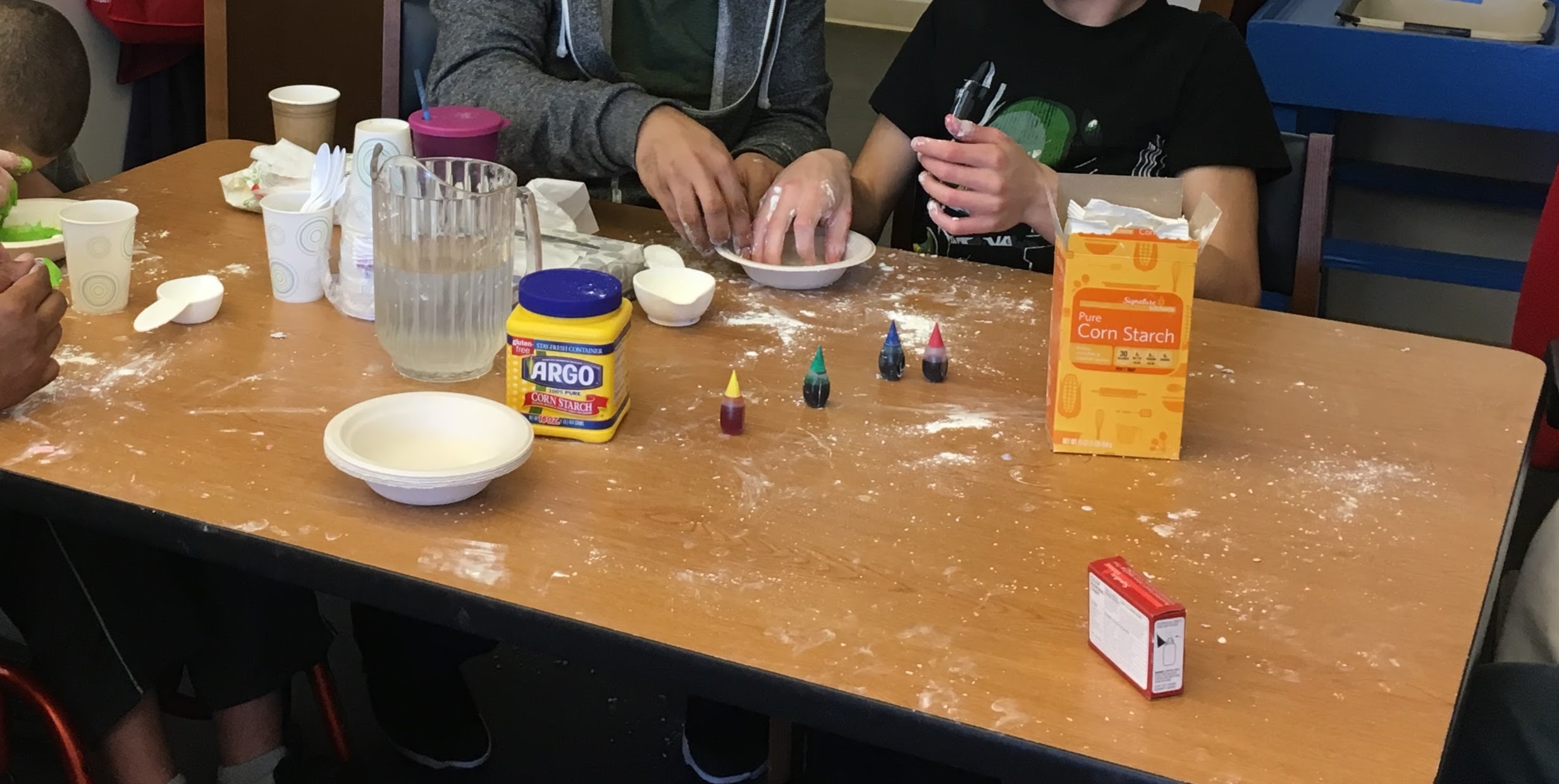 2 people's hands in a bowl with corn starch, watering anf food coloring