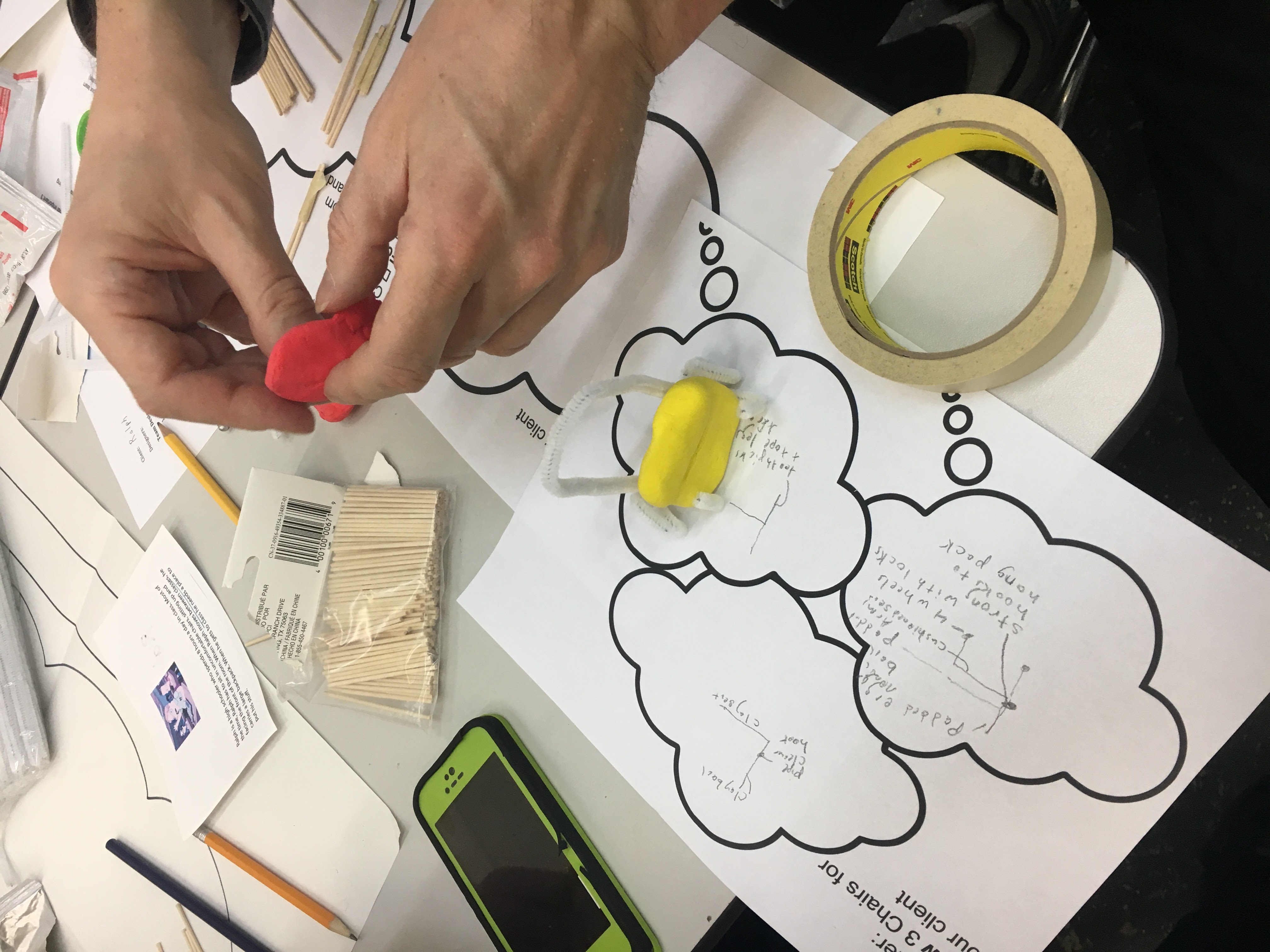 a person forming a lump of play doh over a piece of paper with a thought bubble drawn on