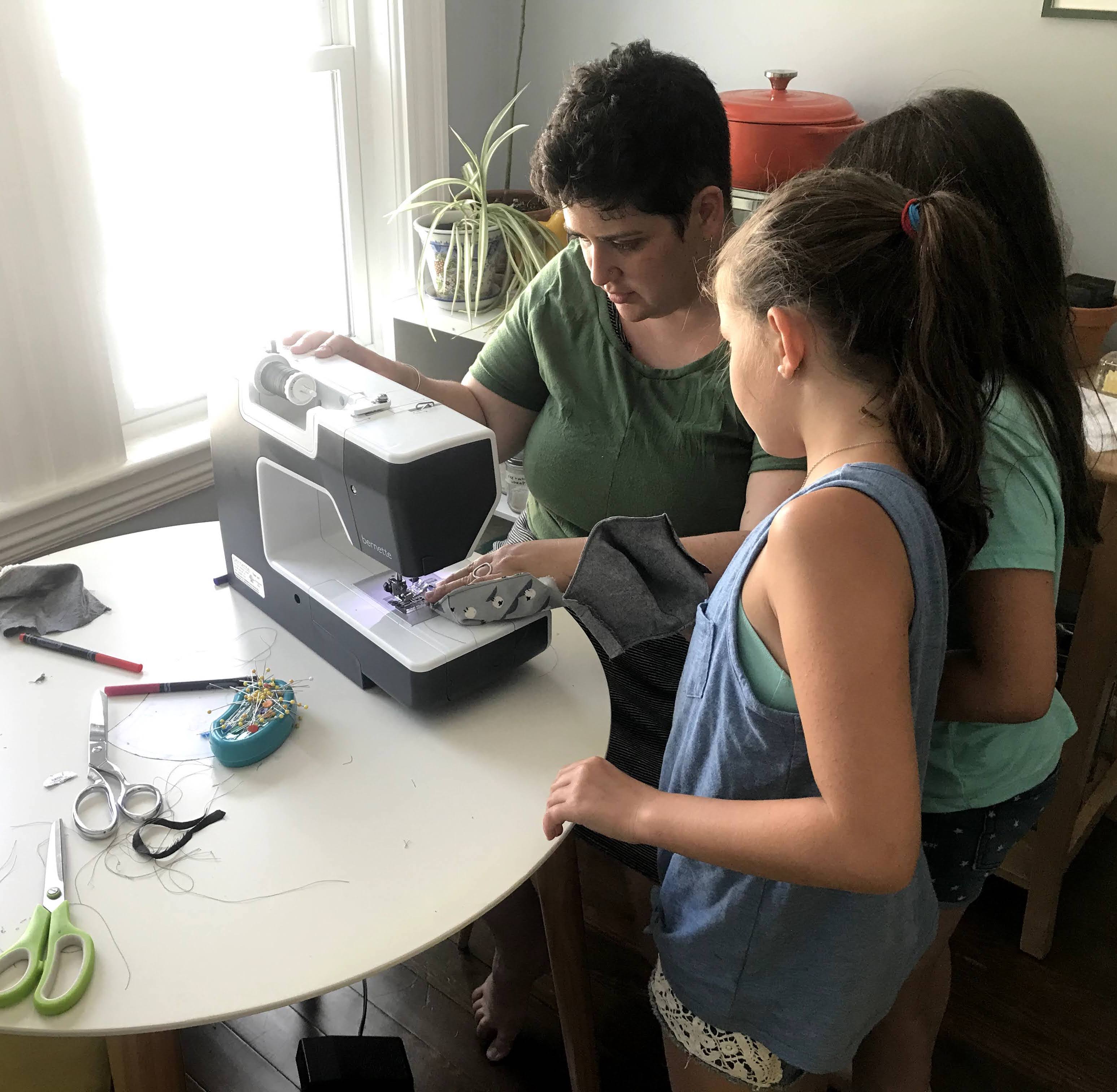 2 children and one adult (Miriam) gathered around a sewing machine