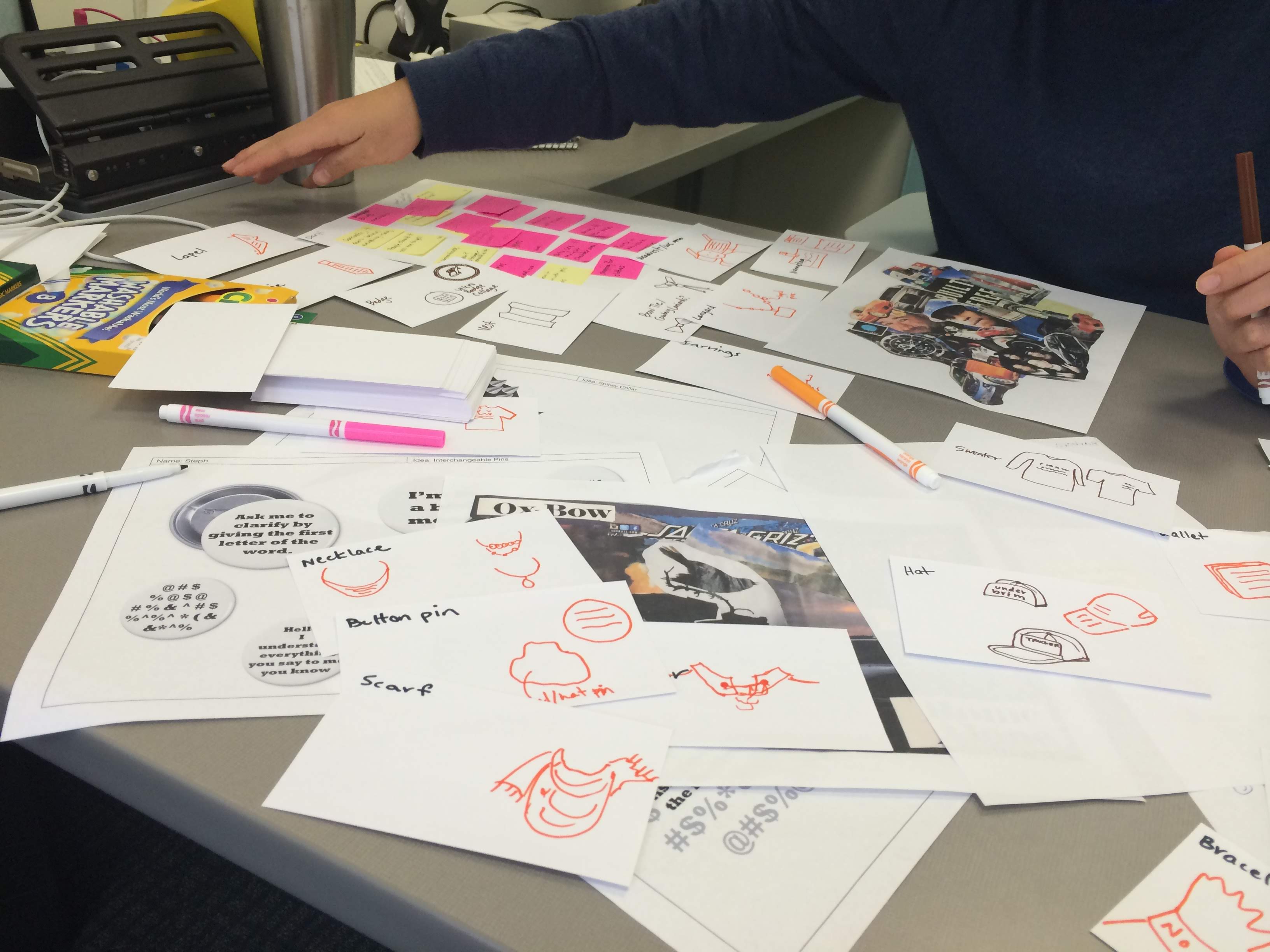 a desk strewn with papers, each with a small sketch, markers and photos scattered throughout